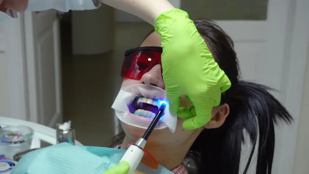 young woman with an expander in mouth and red protective glasses getting uv whitening